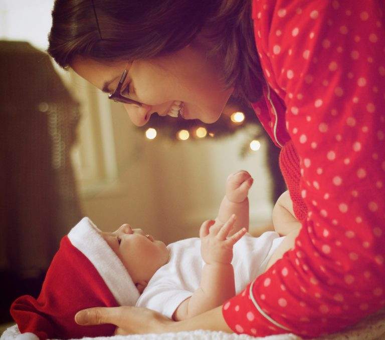 Photo of mother smiling down at a baby in a santa hat.